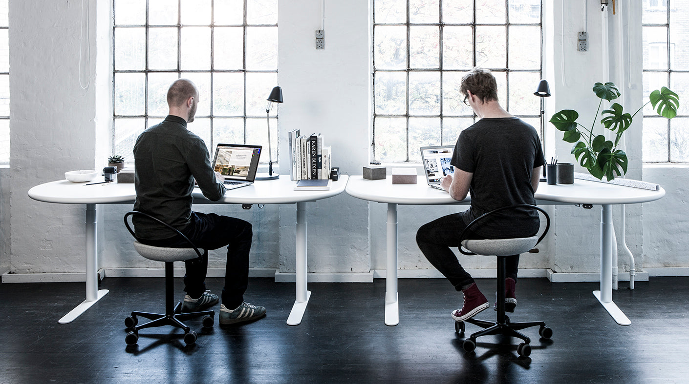 Zwei Männer sitzen und arbeiten an ihren Schreibtischen im Home Office. Beide sitzen auf einem ergonomischen Bürostuhl InCharge Office Black, die Sitze sind mit weißer Hallingdal-Wolle von Kvadrat bezogen.