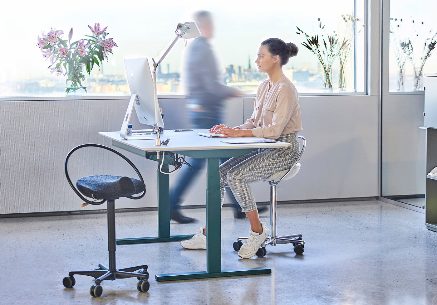 Frau sitzt auf einem ergonomischen Bürostuhl, InCharge Office, bezogen mit hellgrauer Hallingdal-Wolle von Kvadrat. Sie sitzt in einem Büro und arbeitet an ihrem IMac.