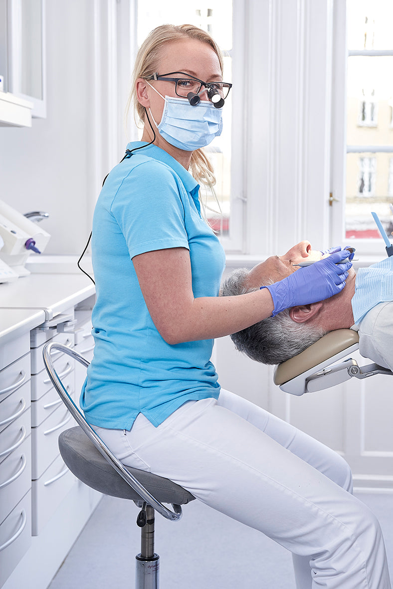 Zahnärztin sitzt auf einem InCharge-Operatorstuhl und arbeitet. Patient liegt im Patientenstuhl.