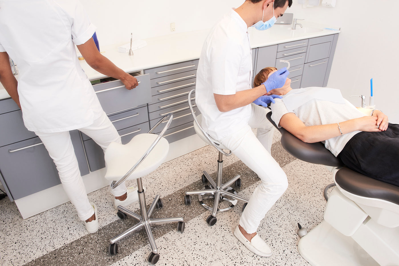Zahnklinik, Zahnarzt sitzt auf ergonomischem InCharge-Stuhl mit Fußsteuerung. Der Klinikassistent steht neben seinem InCharge Behandlungsstuhl. Patient liegt im Patientenstuhl.